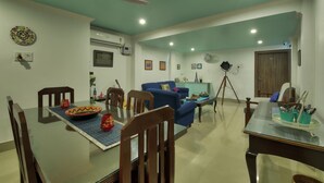 A dining area with a glass table, wooden chairs, and a blue sofa. - Harmony House - A Boutique Hotel (Guwahati)
