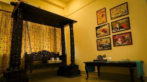 A room with a traditional wooden four-poster bed, a small table with a green cloth, and a wall adorned with vintage posters. - Harmony House - A Boutique Hotel (Guwahati)