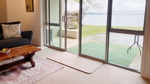 A living room with a sofa, a wooden coffee table, and a sliding glass door leading to a balcony with a view of a body of water. - Lakeside Paradise (Rotorua)