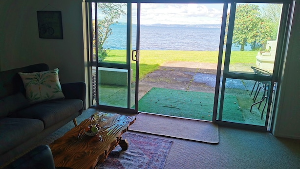 A living room with a sofa, a coffee table, and a view of the sea through glass doors. - Lakeside Paradise (Rotorua)
