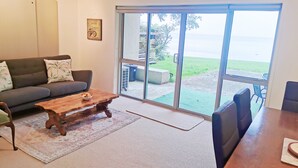 A living room with a sofa, coffee table, and a view through large sliding glass doors to a grassy area. - Lakeside Paradise (Rotorua)