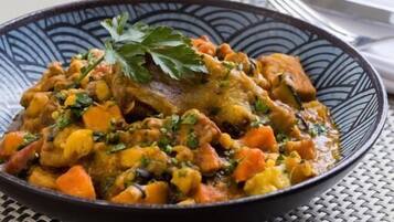 A plate of stew with vegetables and a glass of red wine on a table.