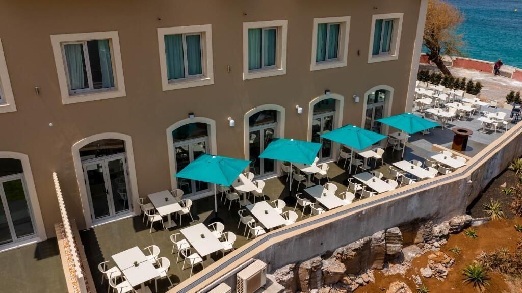 A hotel with outdoor seating areas, multiple windows, and a view of the sea.