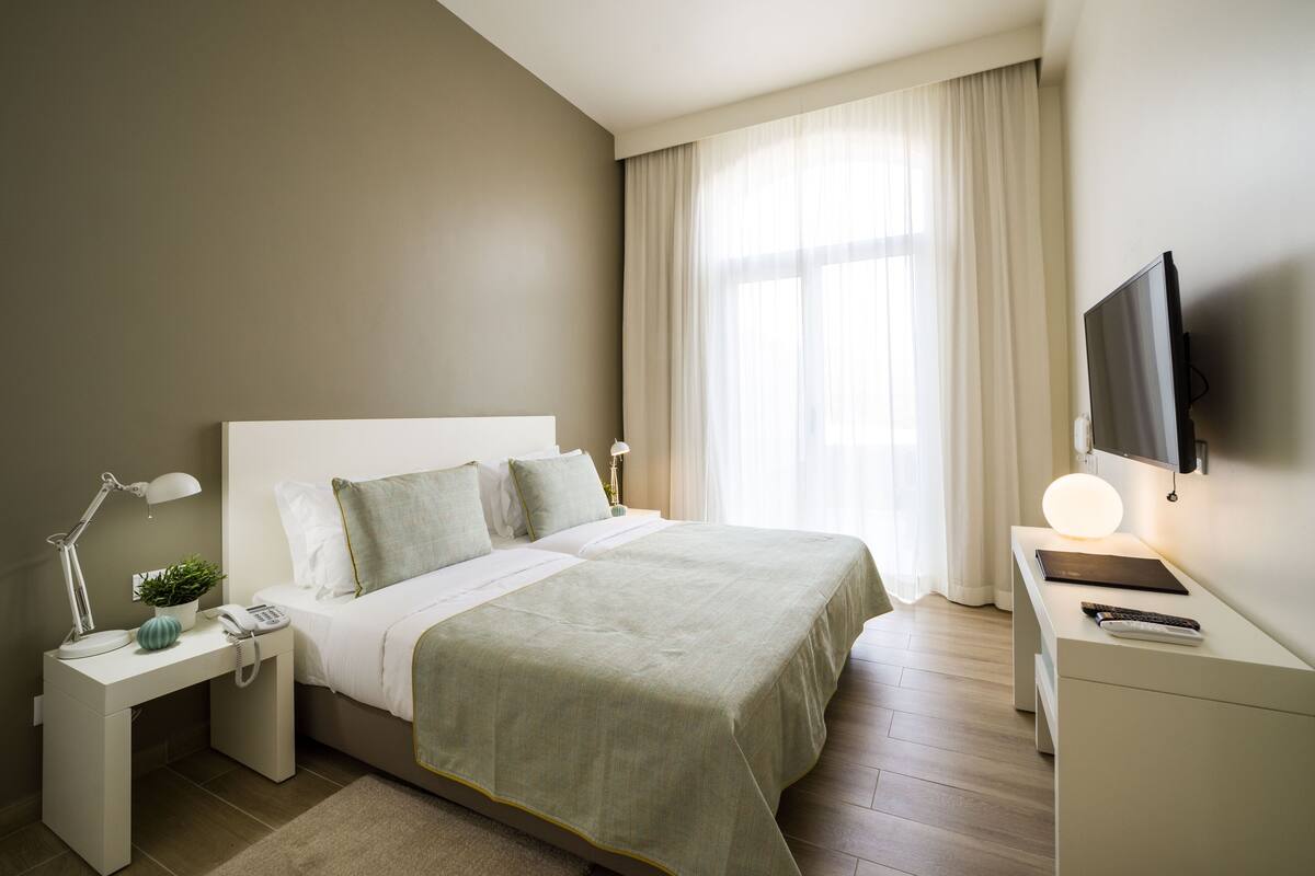 Une chambre à coucher bien rangée, avec un lit, une table de chevet, une lampe et un téléviseur posé sur un meuble.