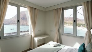 Ein Schlafzimmer mit Bett, Nachttisch und Blick auf das Meer und die Berge.