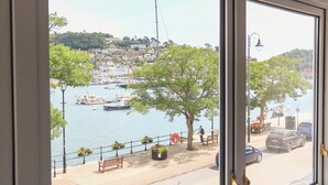 A view of a harbor with boats, a tree-lined promenade, and a building in the background.