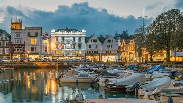 A marina with boats docked, a Royal Castle Hotel, and various buildings along the waterfront.