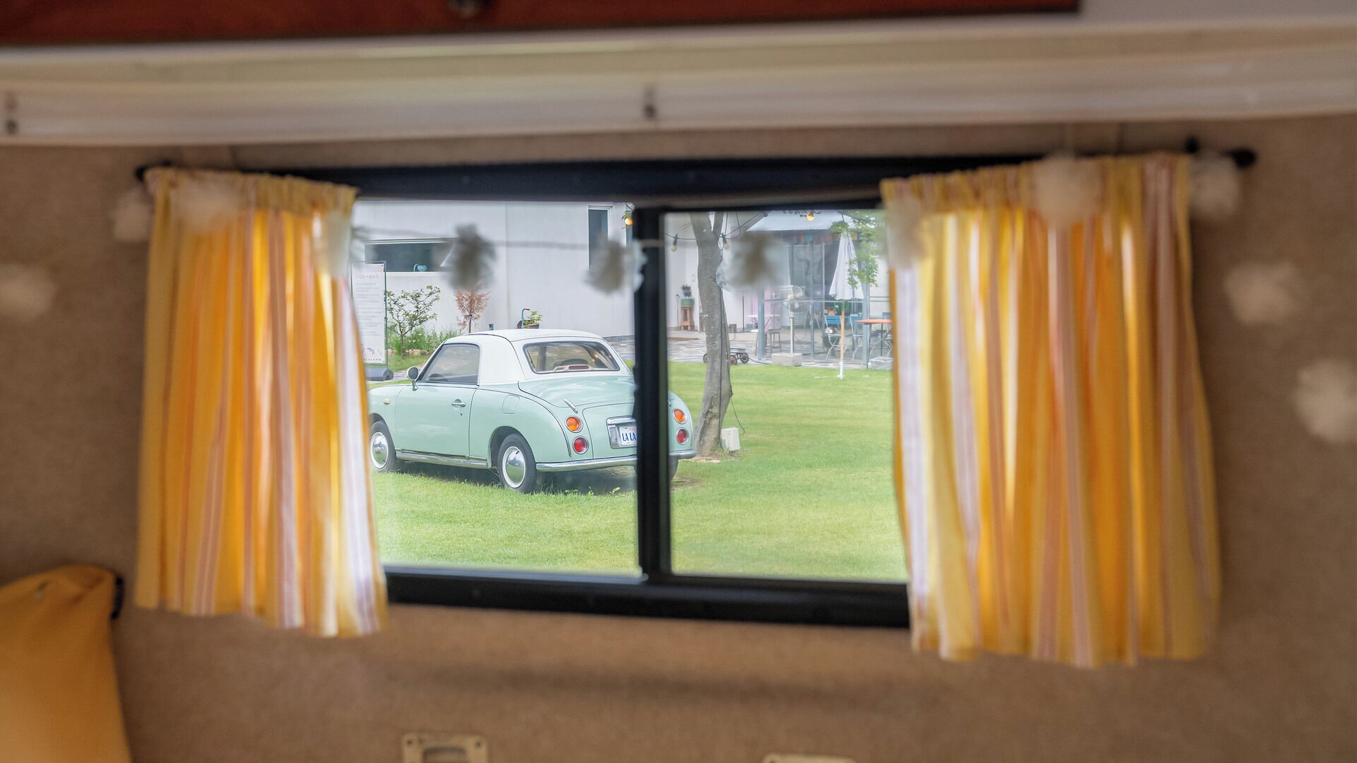 A window with curtains, a view of a parked car outside, and a part of a room interior.