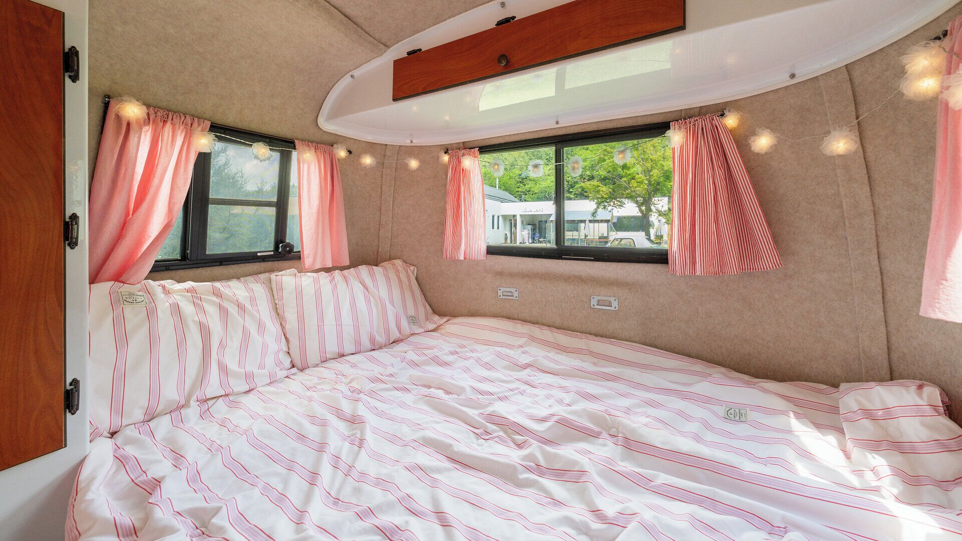 A cozy RV bedroom with a bed, two windows, and curtains.