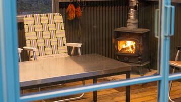 A room with a table, chairs, a striped wall, and a wood-burning stove.