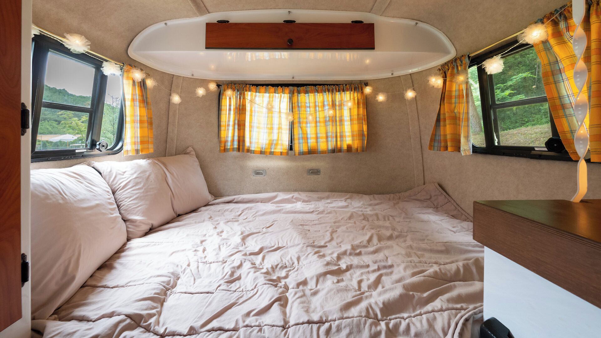 A cozy RV interior with a bed, curtains, and a window with a view.