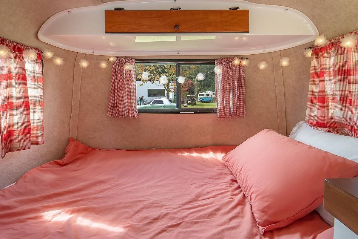 A cozy RV interior with a bed, curtains, and a window view.