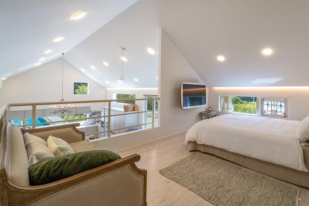 A bedroom with a large bed, a TV, and a balcony with a view of the outdoors.
