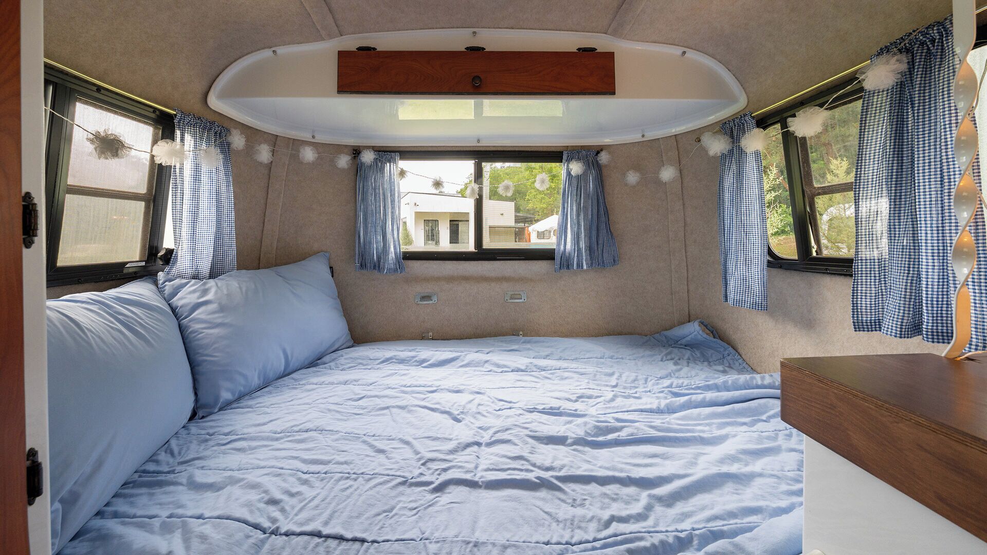 A cozy RV interior with a bed, a small table, and a window with curtains.