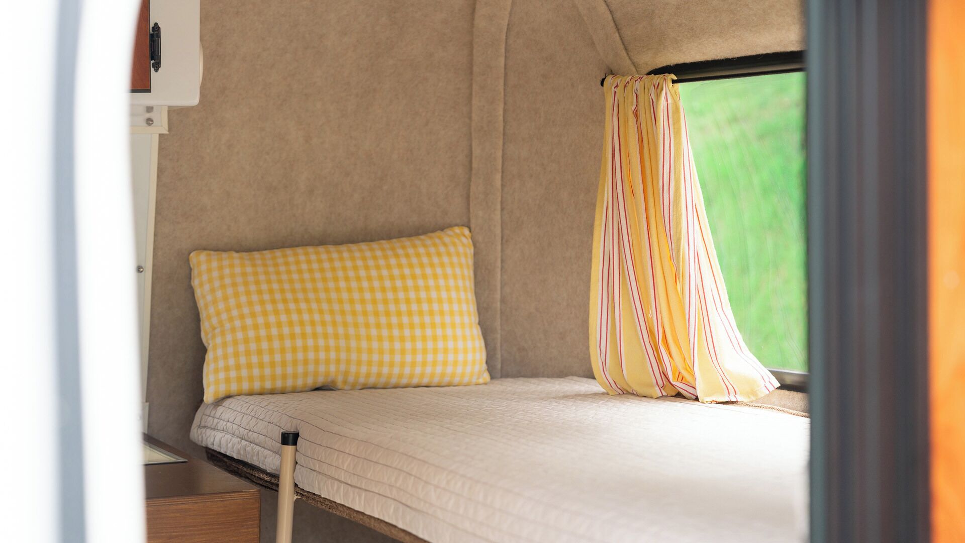A single bed with a checkered pillow and a striped curtain in a tent-like structure.