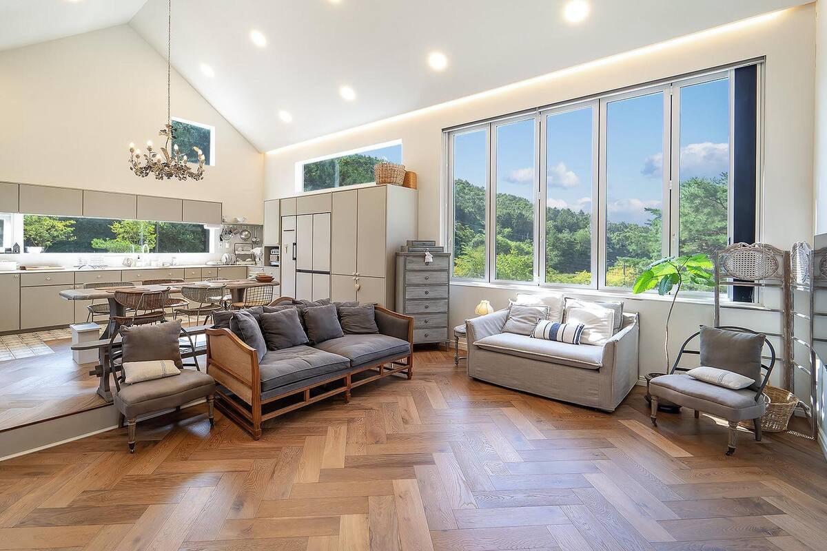 A spacious living area with a large window, a wooden herringbone floor, and a modern kitchen with ample counter space.