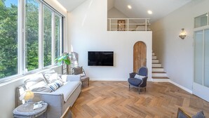Un salon moderne doté d’une grande fenêtre, d’un téléviseur à écran plat, d’un escalier et d’un coin salon confortable.