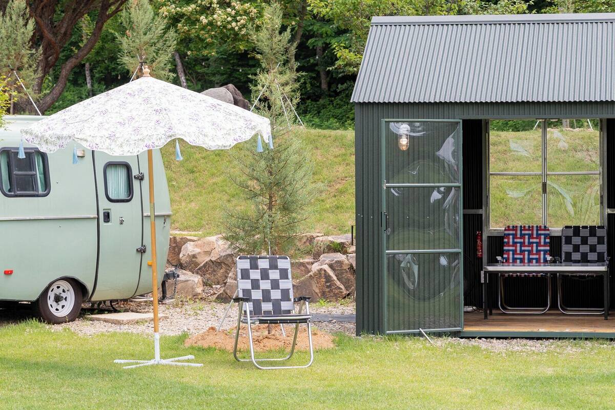 A caravan with a covered outdoor area, a small shed with a bench, and a checkered chair.