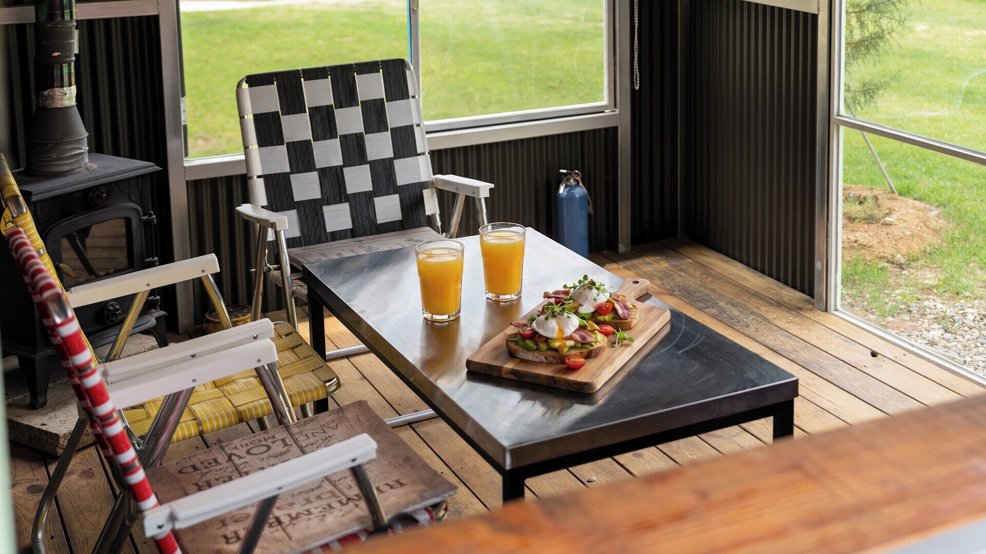 A dining area with a checkered chair, a wooden table, two glasses of orange juice, and a wooden board with a salad.