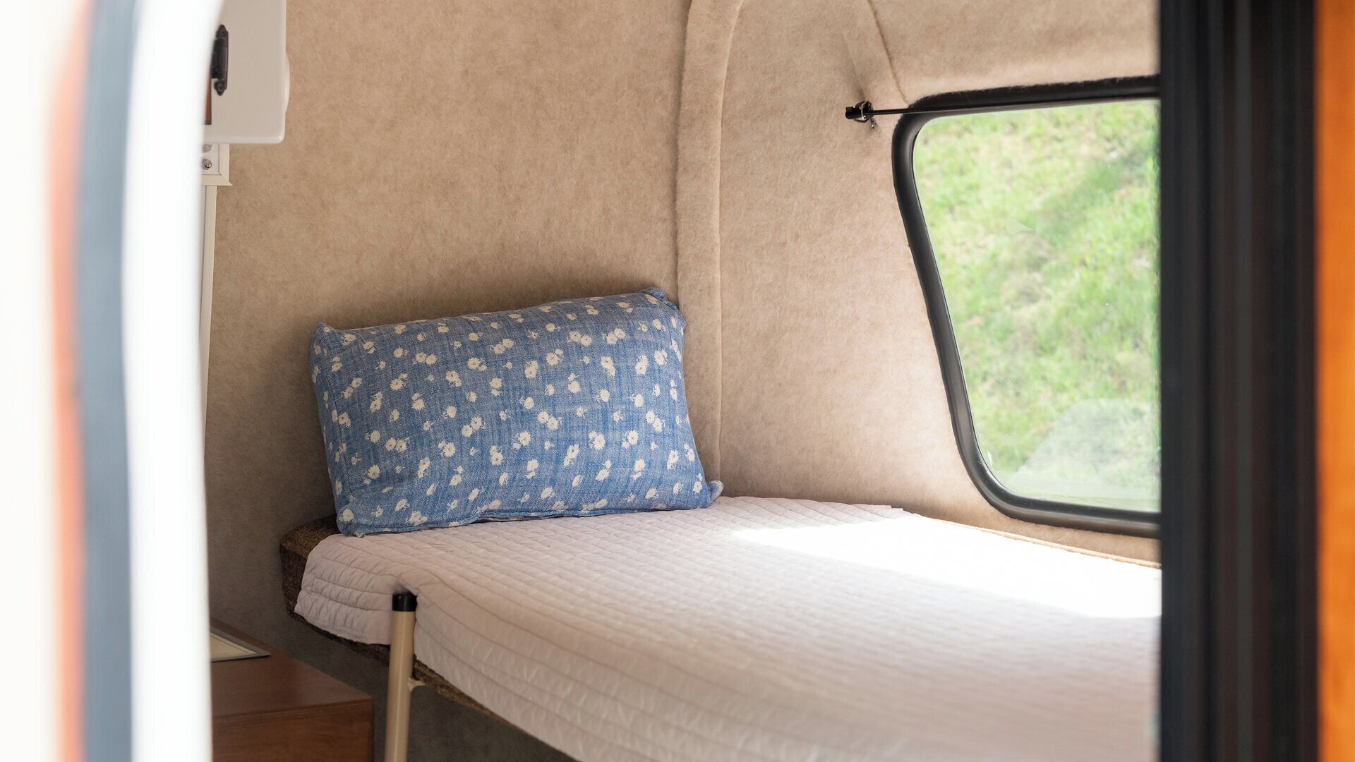 A compact interior with a bed, a window, and a wall-mounted storage unit.