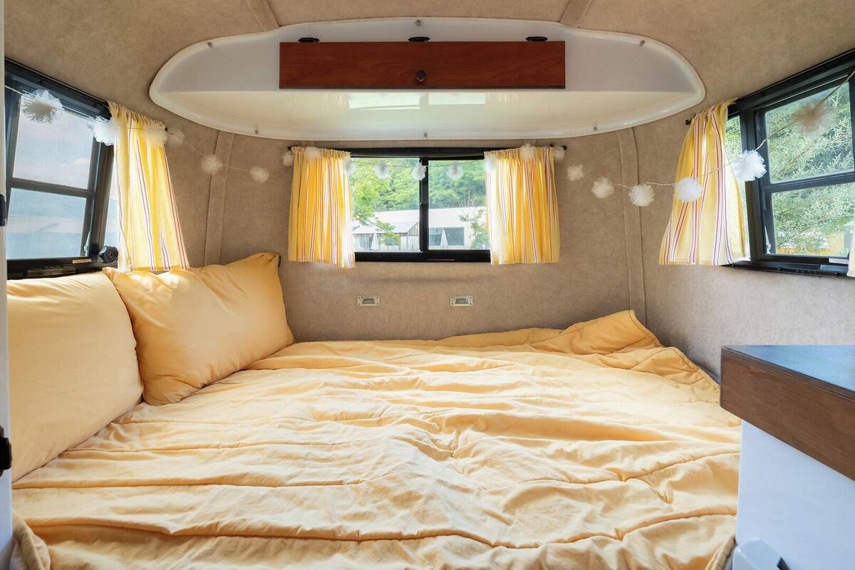 A cozy RV interior with a bed, windows, and a small table.