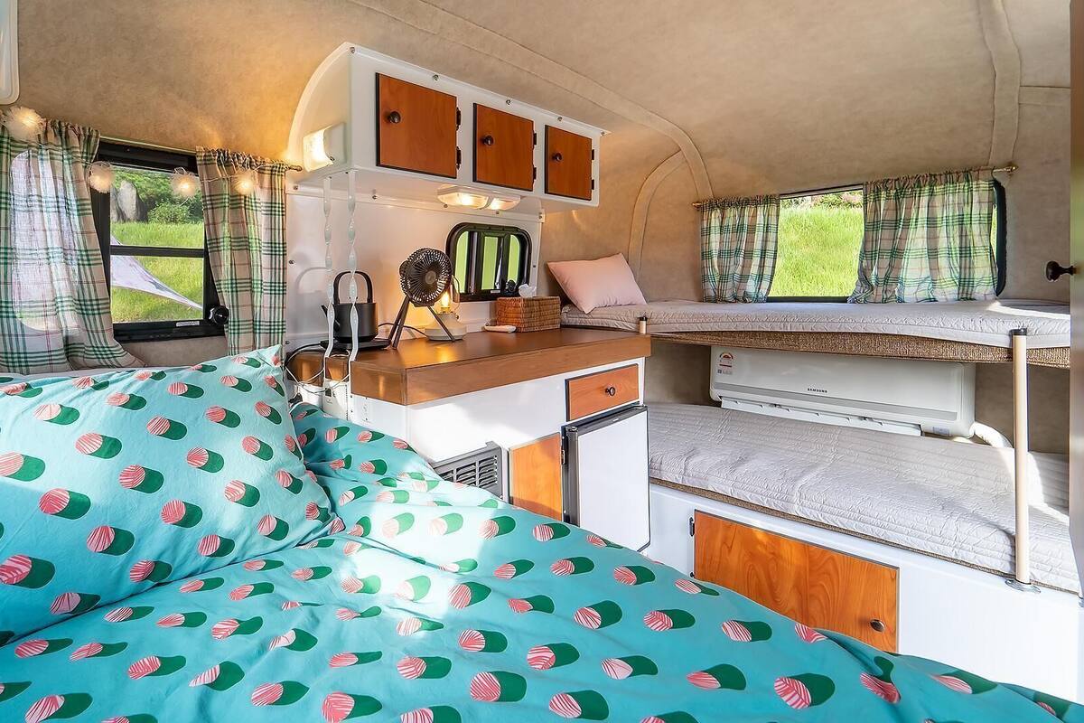 A cozy RV interior with a bed, kitchenette, and a window with curtains.