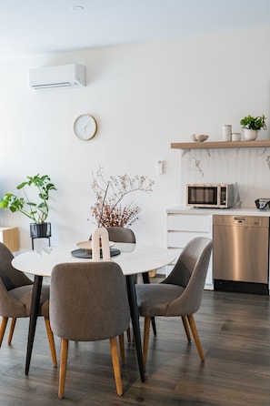 A modern dining area with a round table, grey upholstered chairs, and a white wall-mounted clock.