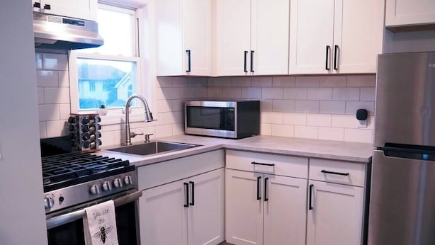A modern kitchen with white cabinets, stainless steel appliances, a microwave, and a gas stove. - Summer Home Close to Beach, Ocean, LIRR w/Balcony (Long Beach)