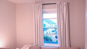 A room with a beige sofa, a wooden side table, and a window with curtains. - Summer Home Close to Beach, Ocean, LIRR w/Balcony (Long Beach)