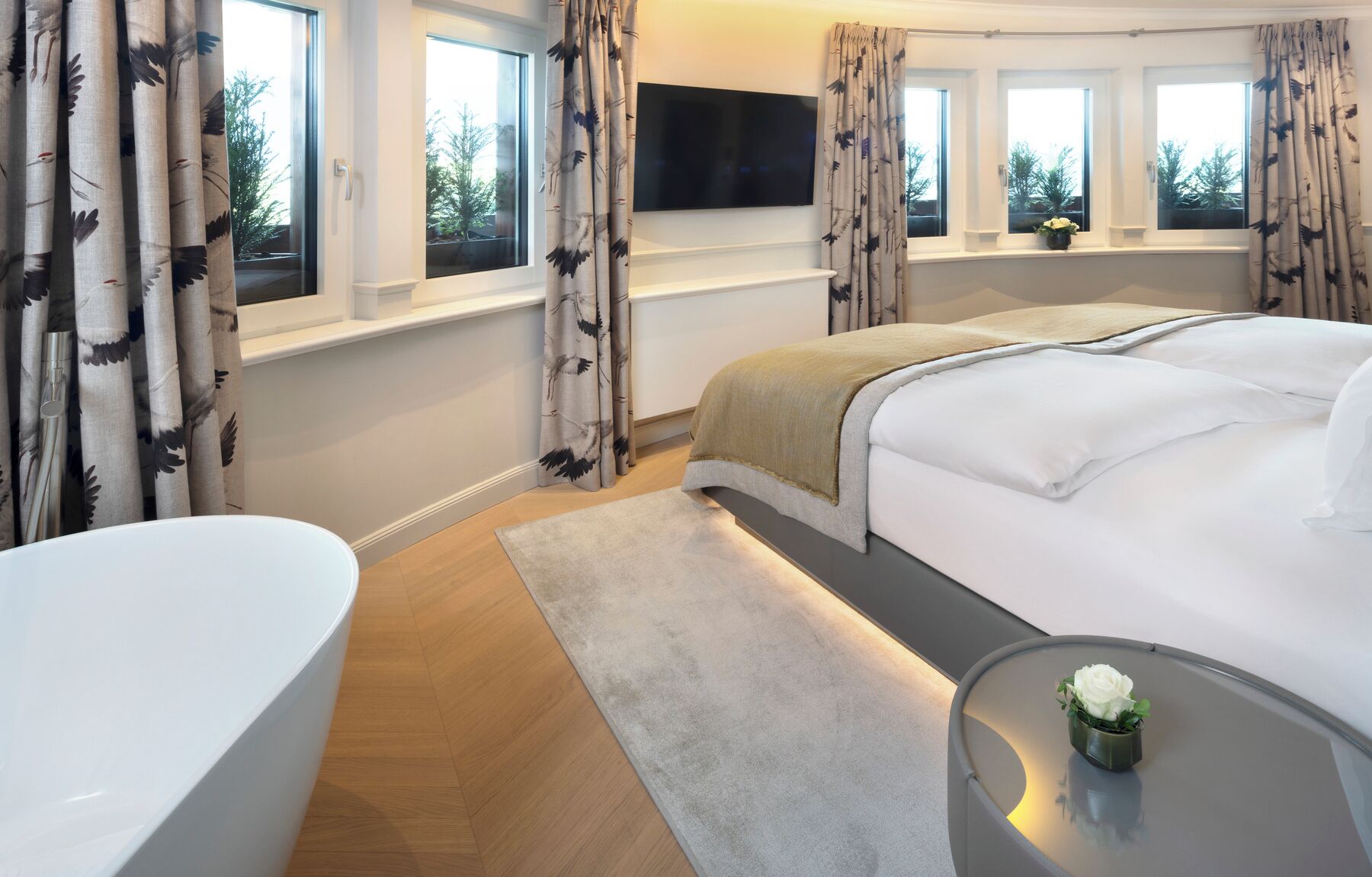 A modern bedroom with a large bed, a TV mounted above it, and a bathtub.