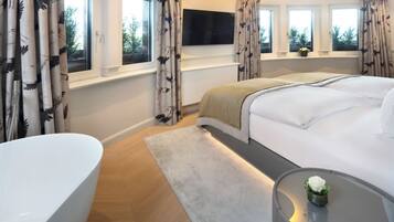 A modern bedroom with a large bed, a TV mounted above it, and a bathtub.