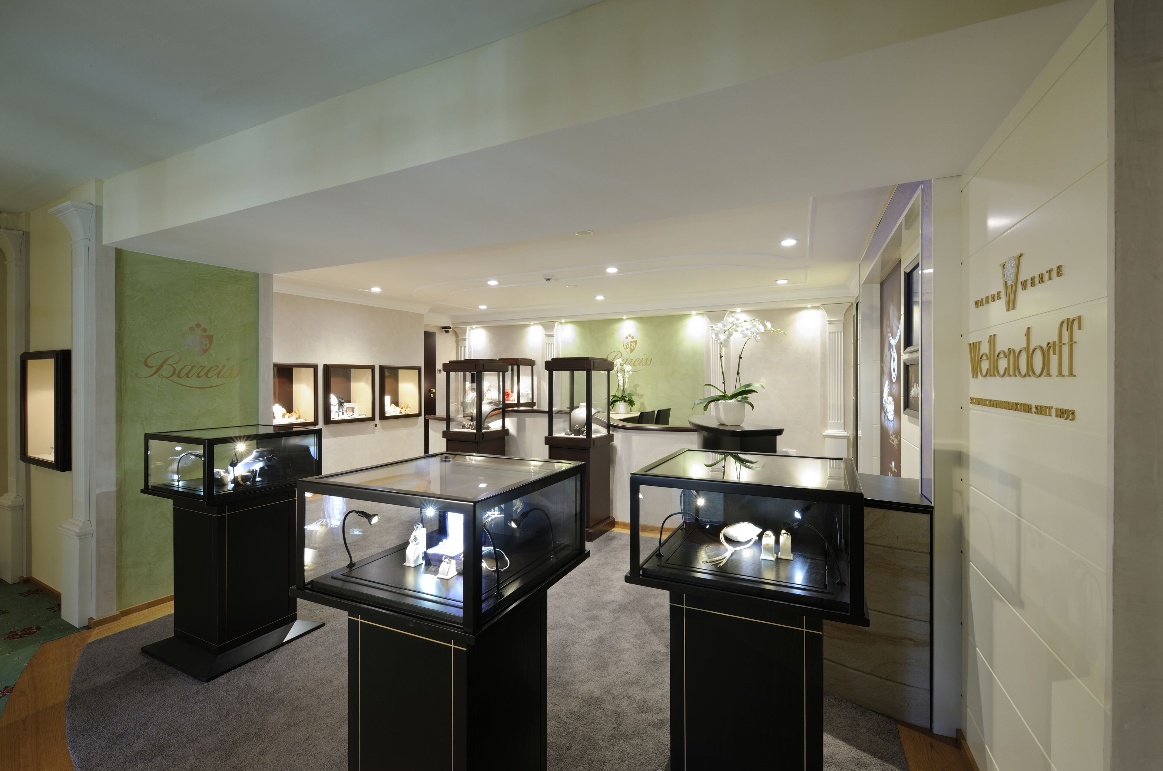 A jewelry display area with glass cases and a green wall with text.