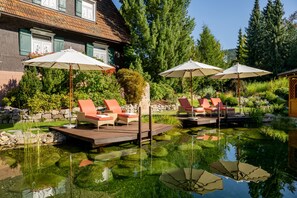 A serene outdoor pool area with lounge chairs and umbrellas, surrounded by lush greenery and a stone wall.
