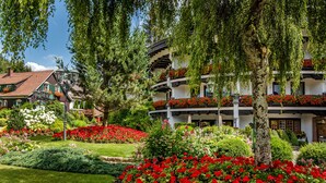 A hotel with a traditional European architectural style, featuring a well-maintained garden with red flowers and green shrubs. - Hotel Bareiss (Baiersbronn)