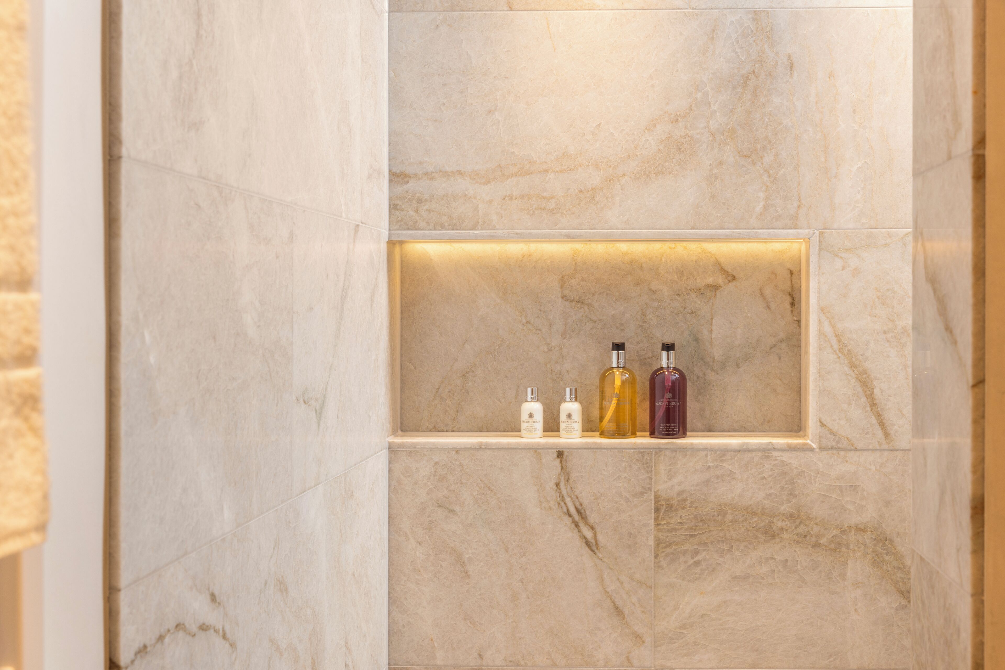 A marble wall with a shelf holding three bottles.