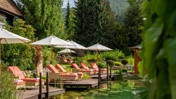 A serene outdoor pool area with lounge chairs and umbrellas, surrounded by lush greenery and a mountainous backdrop. - Hotel Bareiss (Baiersbronn)