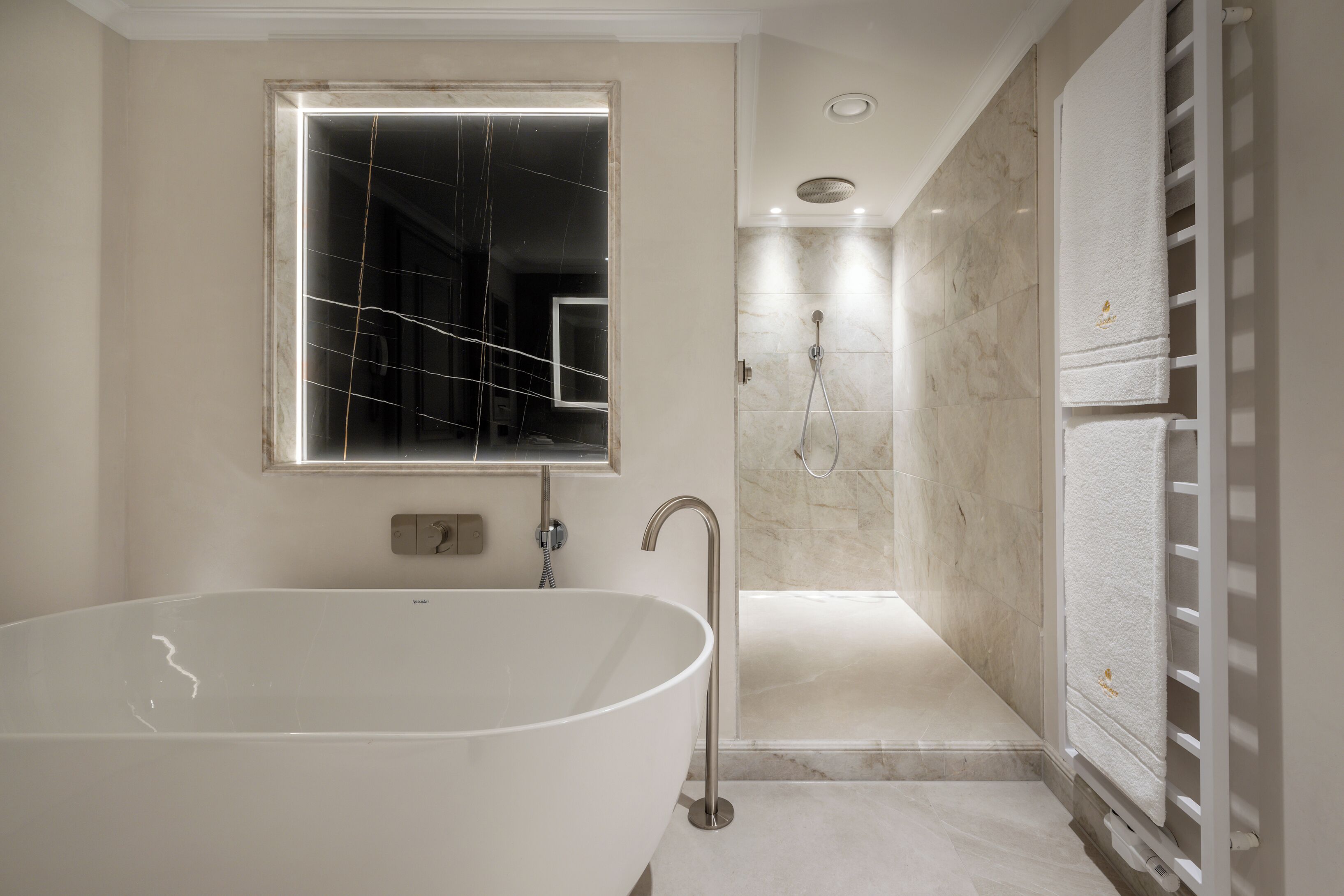 Un baño moderno con una bañera independiente, ducha a ras de suelo y un perchero con toallas dobladas con esmero.