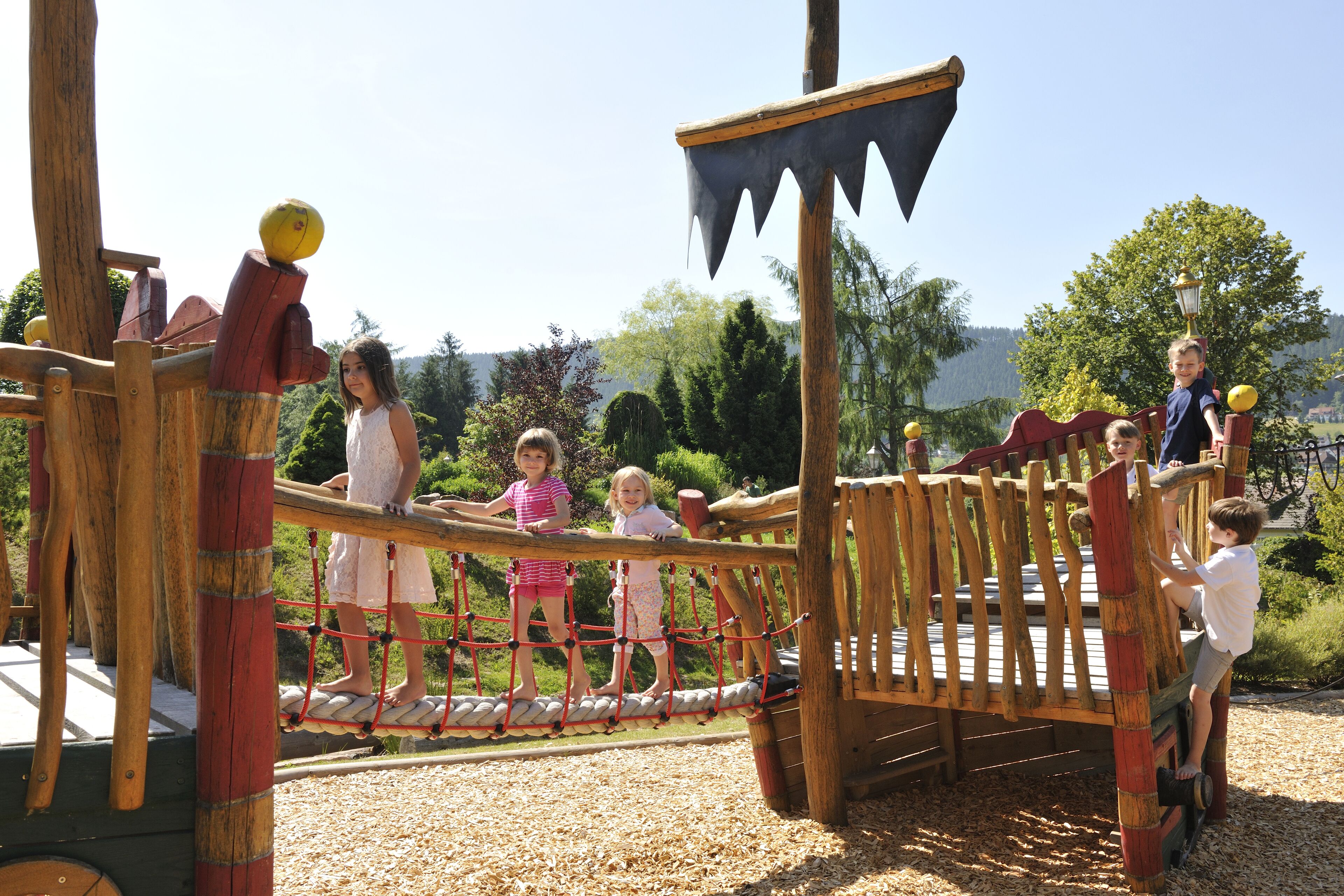Un parque infantil con un puente de cuerda y estructuras de madera.