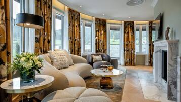 A modern living room with a curved layout, featuring a sofa, armchairs, a coffee table, and a fireplace.
