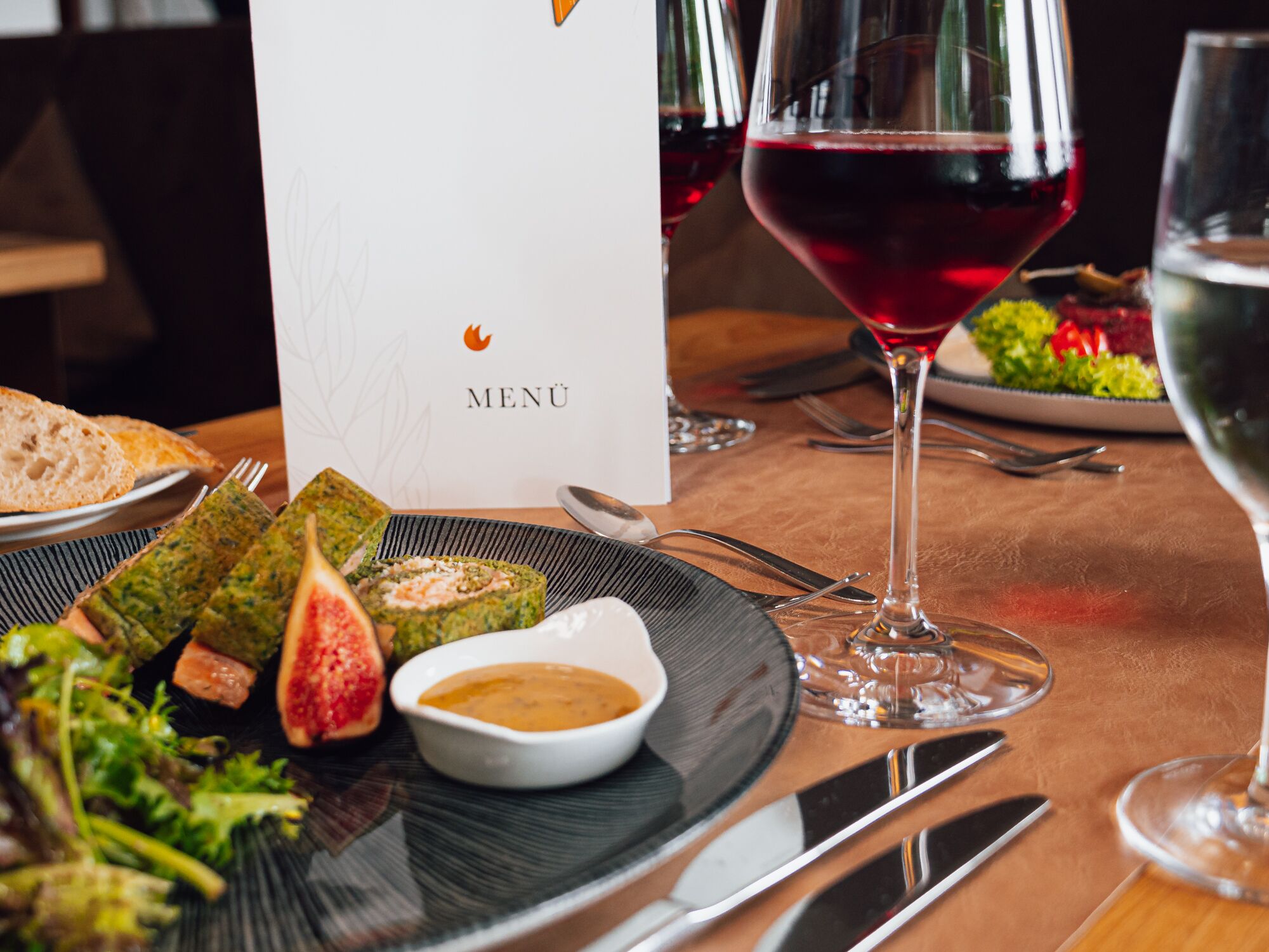 Et spisebord med en menu, et glas rødvin og forskellige retter, heriblandt en salat og en roulade.