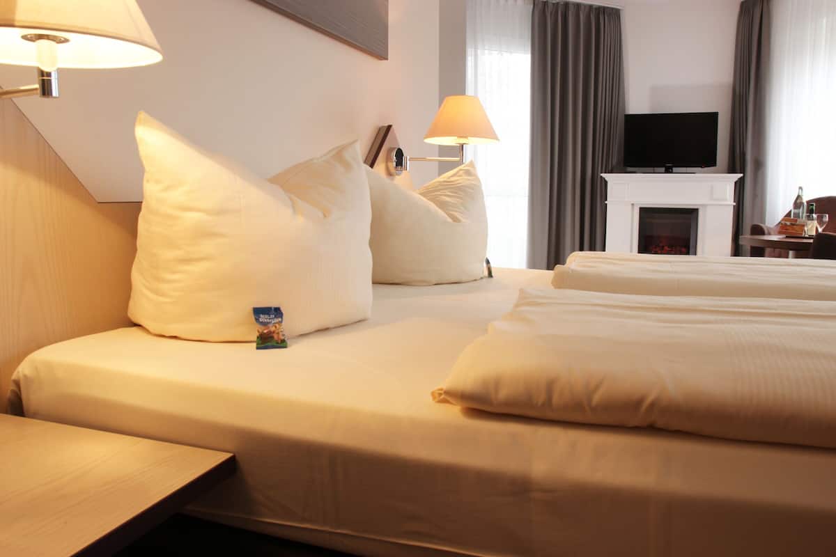 Quarto de hotel com uma cama grande, duas mesas de cabeceira, uma televisão de ecrã plano sobre uma lareira e uma janela com cortinas.