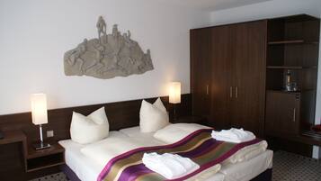 A hotel room with a large bed, two bedside lamps, a wooden wardrobe, and a wall-mounted sculpture.