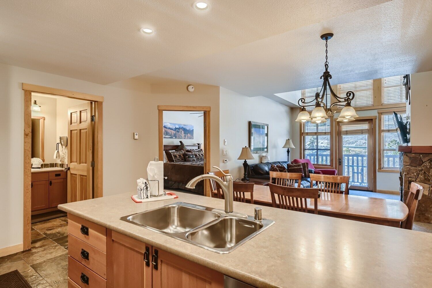 A kitchen with a large island, a dining area with a table and chairs, and a view of a bedroom with a bed and a painting.