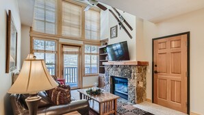 A living room with a fireplace, a television mounted above it, and a door to the right. - Beautiful Top Floor Passage Point 1 Bedroom Condo!! (Copper Mountain)
