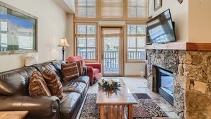 A spacious living room with a leather sofa, a fireplace, and large windows. - Beautiful Top Floor Passage Point 1 Bedroom Condo!! (Copper Mountain)