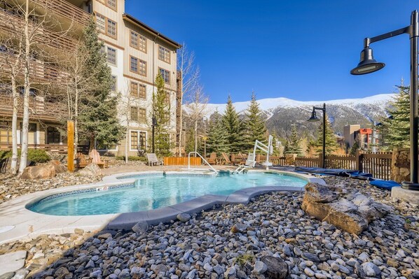 A pool area with a view of mountains, surrounded by trees and a building with multiple windows.