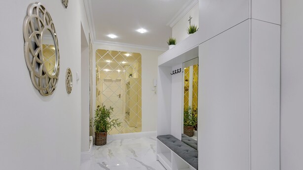 Um corredor com piso de mármore, um banco e espelhos decorativos na parede.