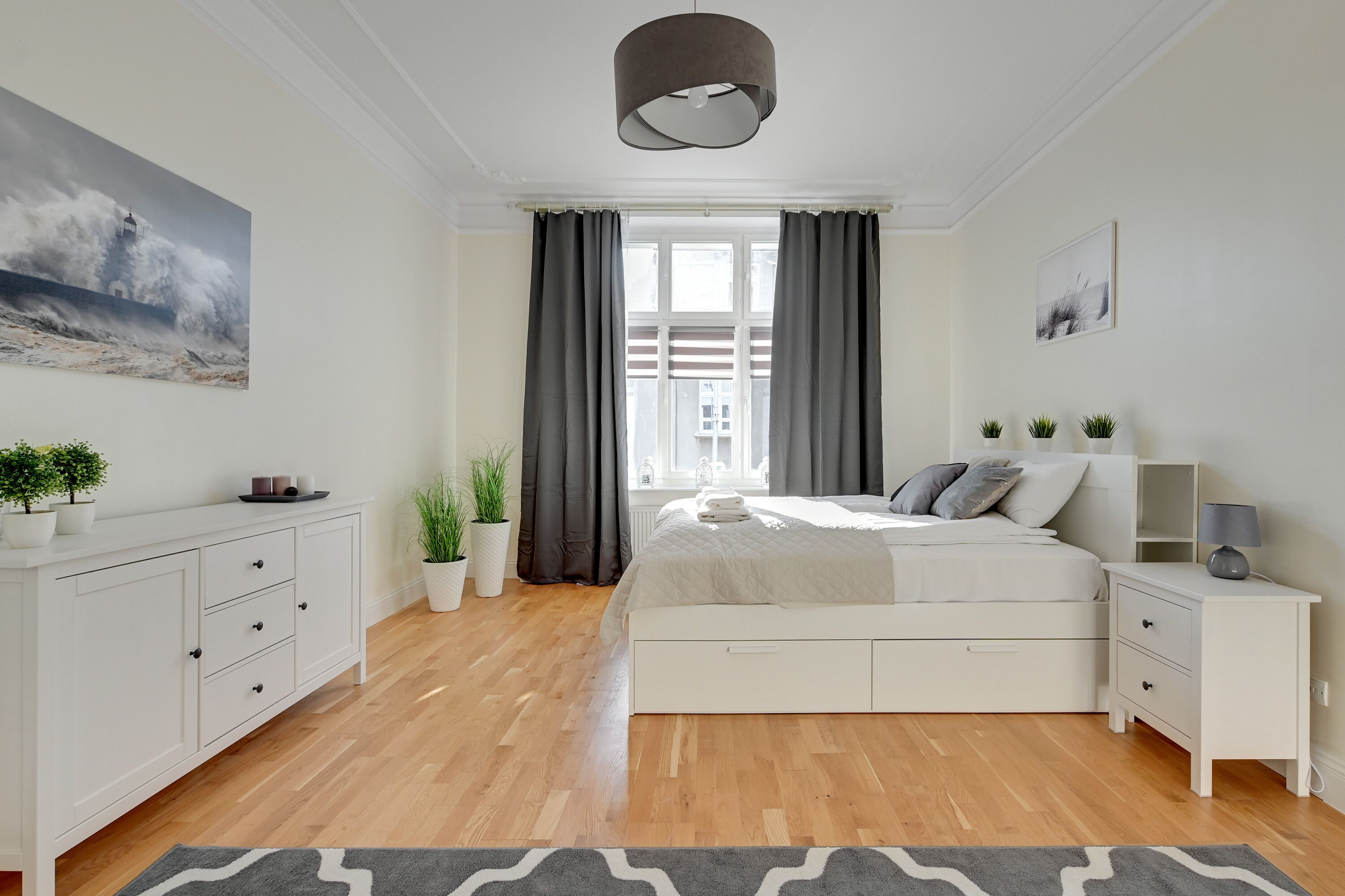 A modern bedroom with a bed, bedside tables, a dresser, and a window with curtains.