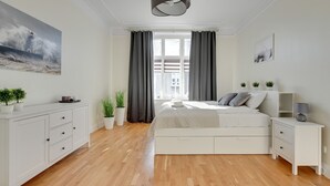 Quarto moderno com cama, mesas de cabeceira, cômoda e janela com cortinas.