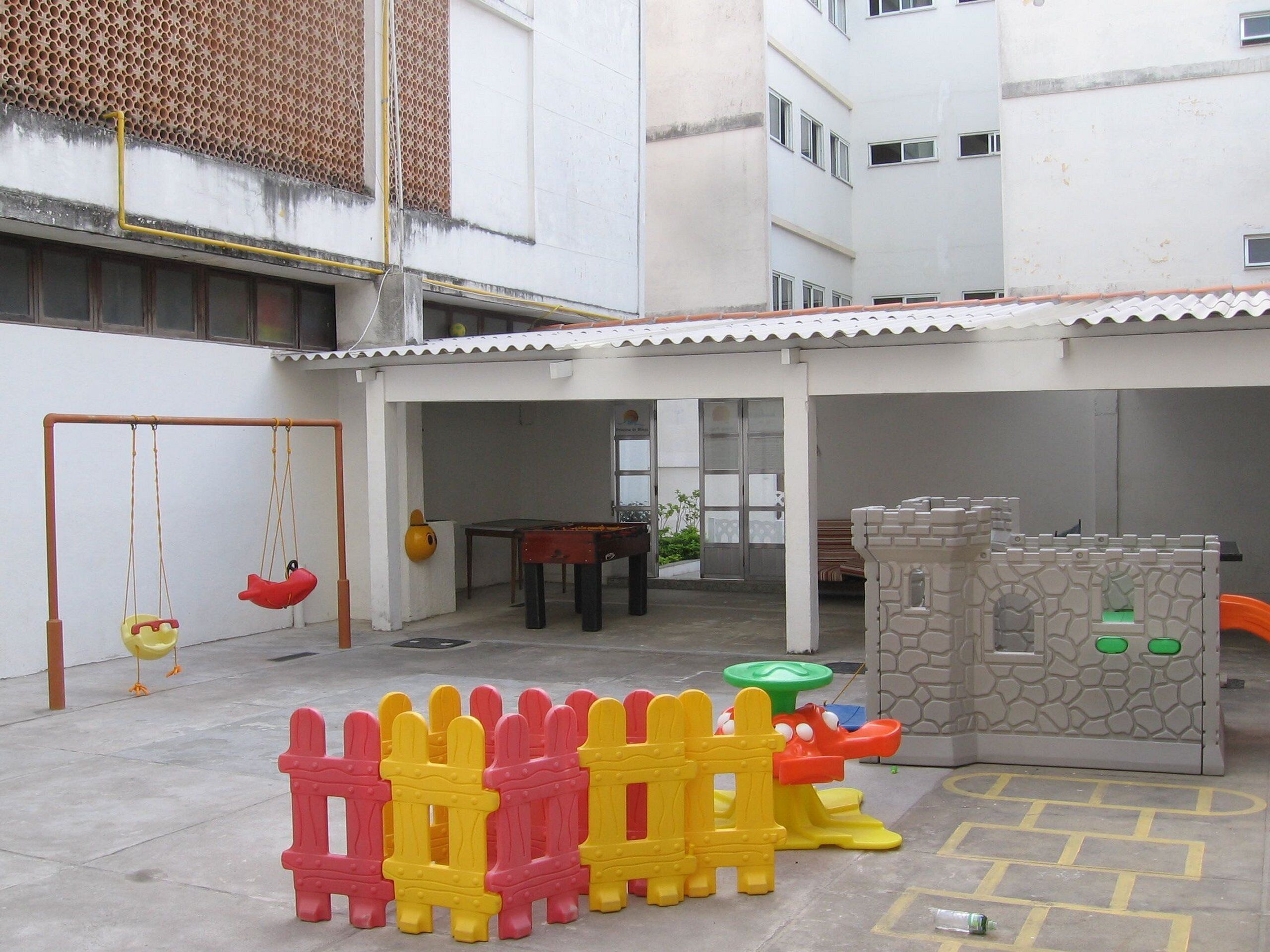 Espaço infantil com baloiço, mesa de bilhar pequena e estrutura de diversões em formato de castelo.